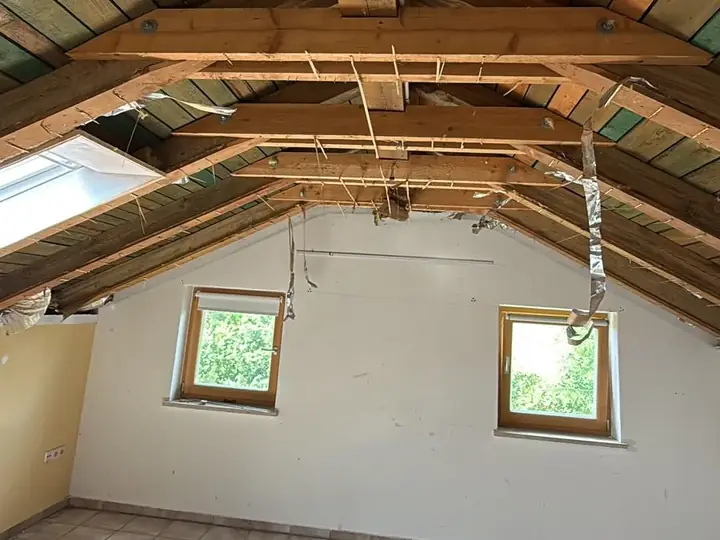 Dachgeschoss vor dem Ausbau: offener Dachstuhl mit alter Holzschalung, Giebelwand mit zwei Fenstern