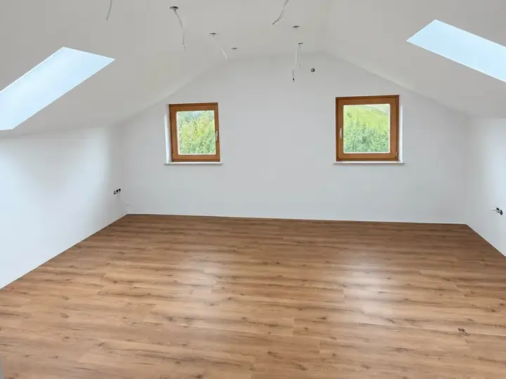 Dachgeschoss nach dem Ausbau: weiße Wände und Dachschrägen, zwei Dachfenster, Boden in Holzoptik