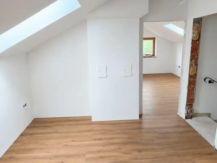 Dachgeschoss nach der Sanierung: weiße Wände und Schrägen, Dachfenster, Durchgang zum Nachbarraum, Boden in Holzoptik